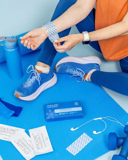 A woman in running shoes on a blue yoga mat, pressing an Endure cooling patch onto her wrist, with a box of patches beside her.